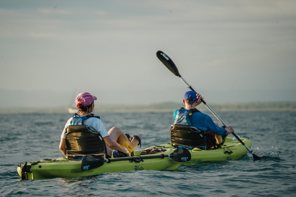 Two person ocean kayak with a passenger raising their paddle