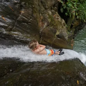 Child sliding down a natural waterfall in Costa Rica during a family tour